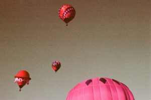 four hot air balloons raise into a cloudless sky. everything is tinged purple, due to the purple-cast of the film the photo was shot on